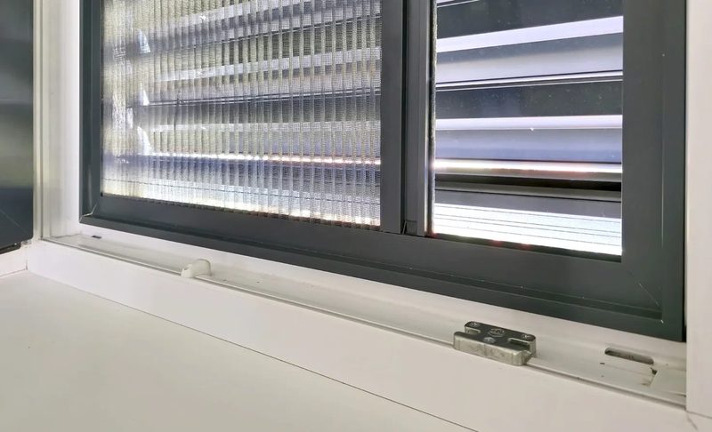Uchycení sítě proti hmyzu na spodním rámu okna zblízka, vedle otevřené okenní křídlo